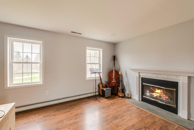 unfurnished living room featuring visible vents, light wood finished floors, a glass covered fireplace, and baseboard heating