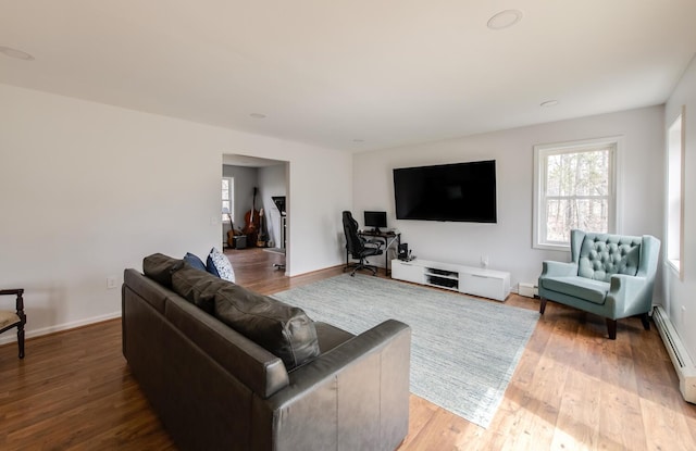 living area featuring baseboards, a baseboard heating unit, wood finished floors, and a wealth of natural light