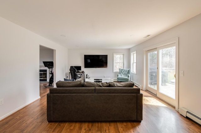 living area with baseboard heating, baseboards, visible vents, and wood finished floors
