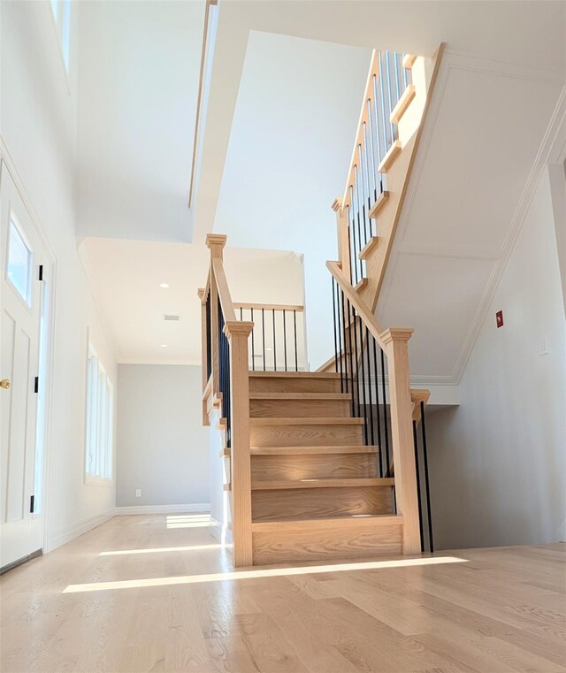 1135 Logan Rd, Wantagh, NY 11793 - stairway featuring wood finished floors, healthy amount of natural light, crown molding, and a towering ceiling