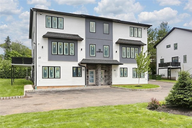 view of front of house featuring aphalt driveway, stone siding, a shingled roof, and a front yard