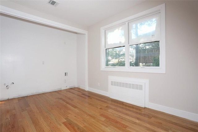 empty room with visible vents, radiator heating unit, light wood-type flooring, and baseboards