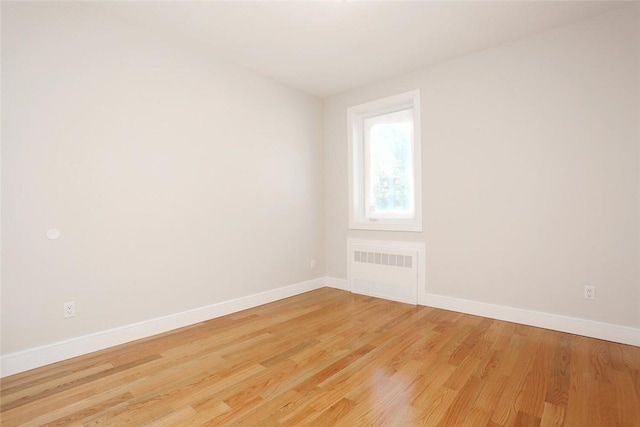 empty room with radiator heating unit, light wood finished floors, and baseboards