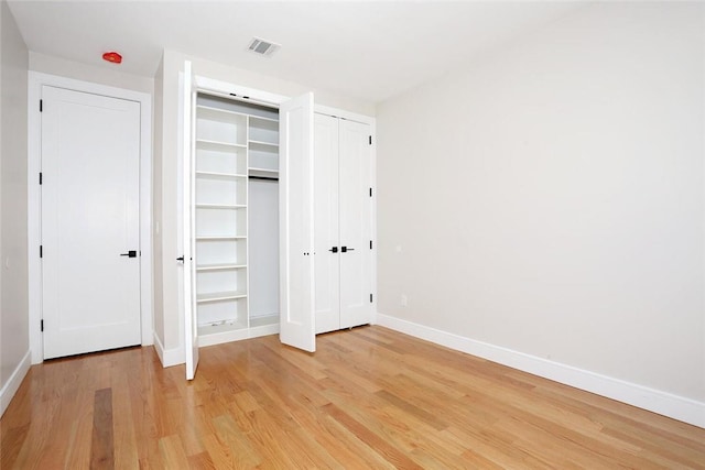 unfurnished bedroom with multiple closets, visible vents, baseboards, and light wood finished floors