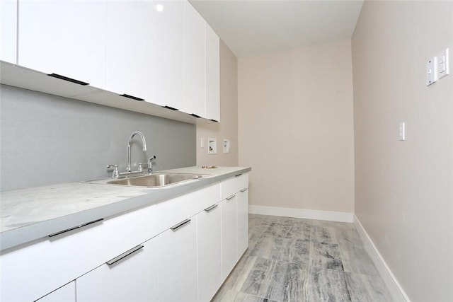 interior space featuring baseboards, light wood-style flooring, hookup for a washing machine, cabinet space, and a sink