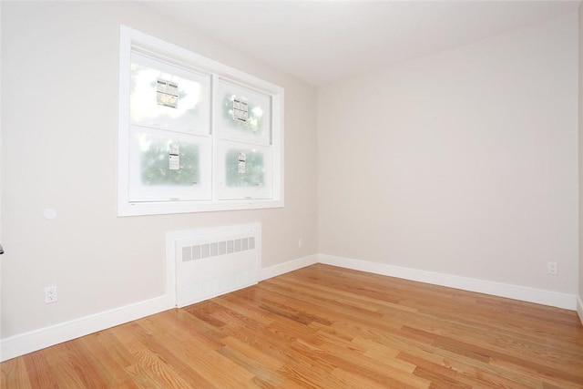 unfurnished room with radiator heating unit, light wood-style flooring, and baseboards