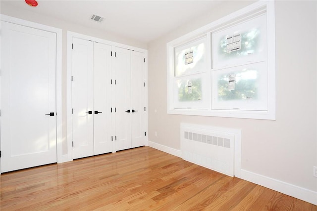 unfurnished bedroom featuring radiator, visible vents, multiple closets, light wood finished floors, and baseboards