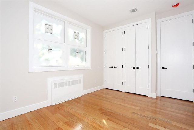 unfurnished bedroom with baseboards, light wood-type flooring, radiator, and two closets