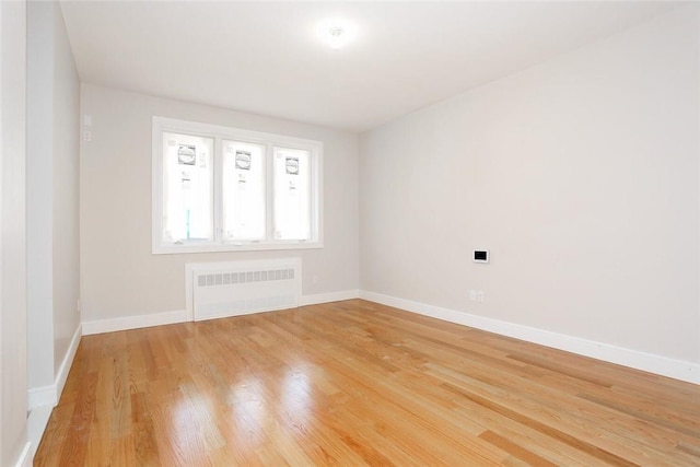 unfurnished room with radiator heating unit, light wood finished floors, and baseboards