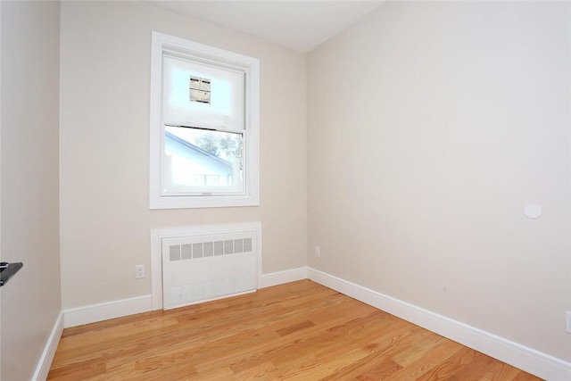 empty room featuring light wood-style flooring, radiator heating unit, and baseboards