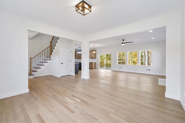 unfurnished living room with ceiling fan, light wood-style flooring, visible vents, stairway, and baseboards