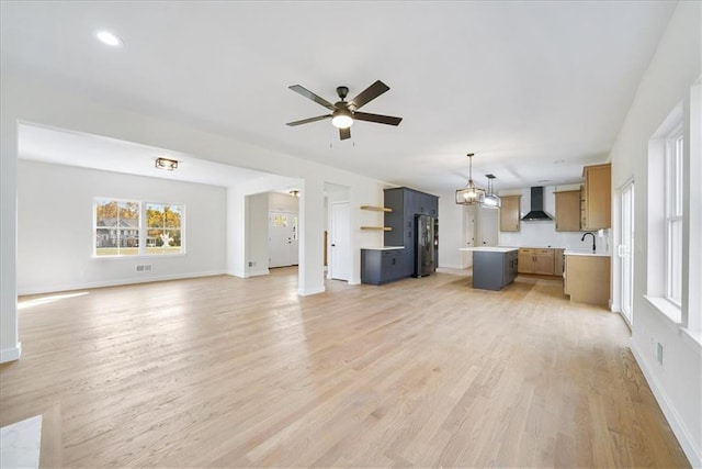 unfurnished living room featuring ceiling fan with notable chandelier, light wood finished floors, a sink, and baseboards