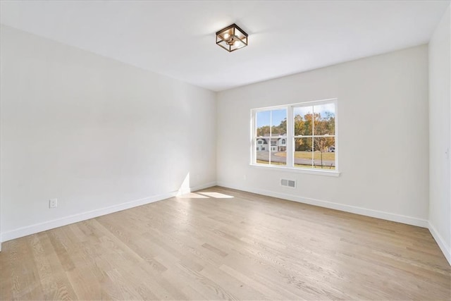 empty room with visible vents, light wood-type flooring, and baseboards