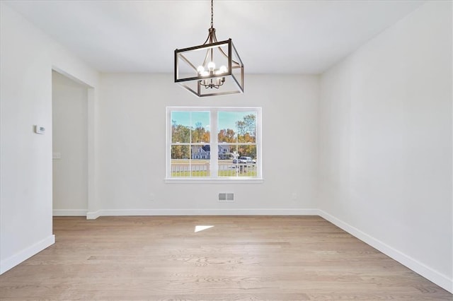 unfurnished room with visible vents, light wood-style flooring, an inviting chandelier, and baseboards
