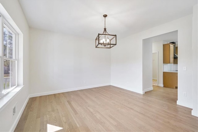 unfurnished room featuring baseboards, light wood finished floors, plenty of natural light, and a notable chandelier