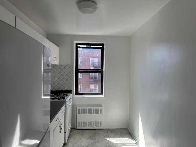 kitchen featuring white cabinetry, freestanding refrigerator, radiator heating unit, white range with gas stovetop, and marble finish floor