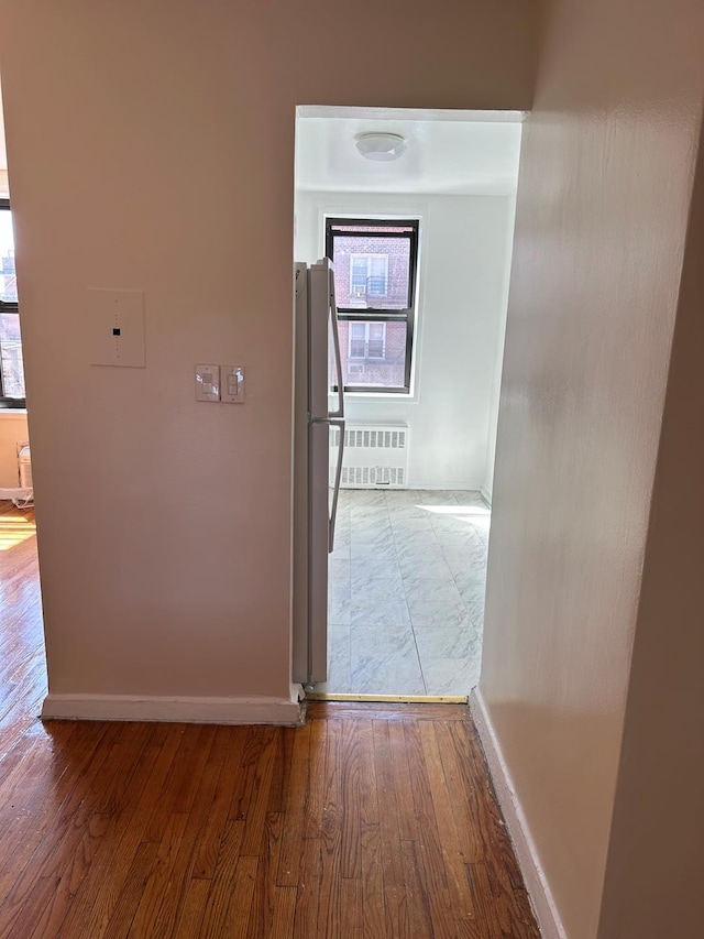 corridor with radiator heating unit, wood finished floors, and baseboards