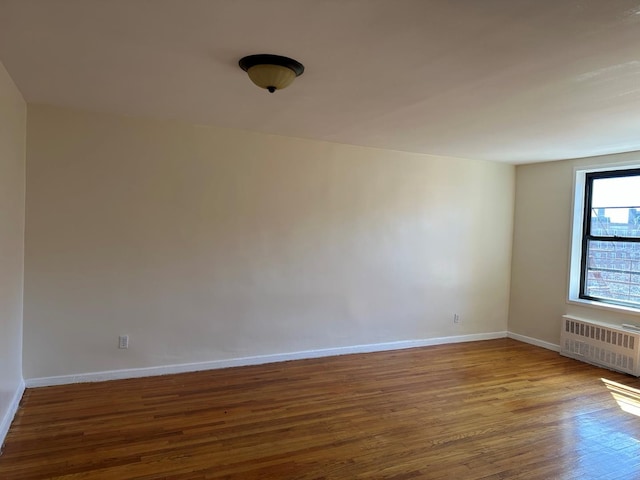 empty room with radiator heating unit, wood finished floors, and baseboards