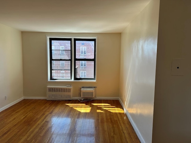 unfurnished room featuring radiator heating unit, baseboards, a wall unit AC, and wood finished floors