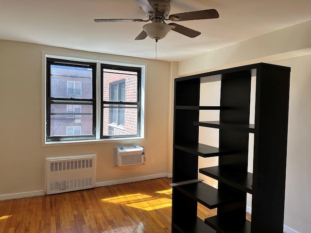 spare room with baseboards, ceiling fan, a wall mounted AC, wood finished floors, and radiator heating unit