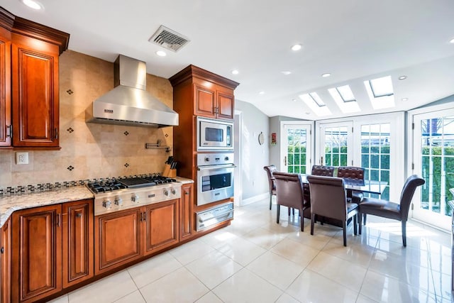 34 Duke Dr, Manhasset Hills, NY 11040 - kitchen featuring wall chimney range hood, tasteful backsplash, brown cabinetry, stainless steel appliances, and visible vents