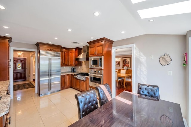34 Duke Dr, Manhasset Hills, NY 11040 - kitchen featuring light stone counters, brown cabinets, decorative backsplash, built in appliances, and wall chimney exhaust hood