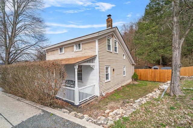 view of property exterior featuring a porch, a chimney, and fence