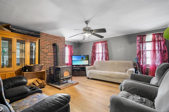 living room featuring crown molding, a wood stove, a ceiling fan, and wood finished floors