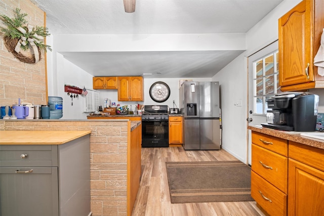 kitchen with brown cabinetry, light wood-style floors, stainless steel fridge with ice dispenser, and black gas range oven