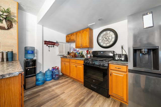 kitchen featuring black range with gas stovetop, light wood-style flooring, dark countertops, stainless steel refrigerator with ice dispenser, and brown cabinets