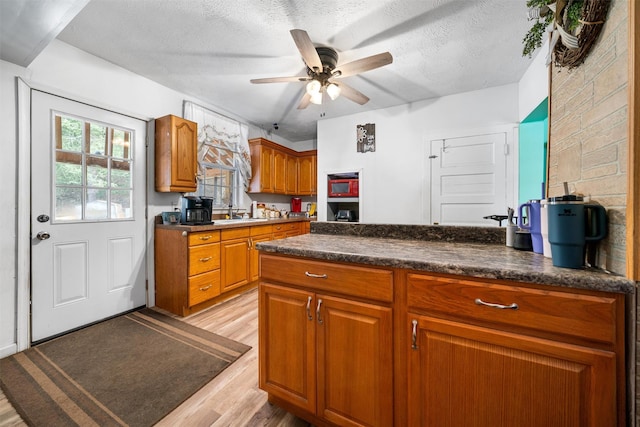 kitchen with a textured ceiling, a ceiling fan, dark countertops, brown cabinets, and light wood finished floors