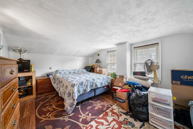 bedroom with wood finished floors, vaulted ceiling, and a textured ceiling