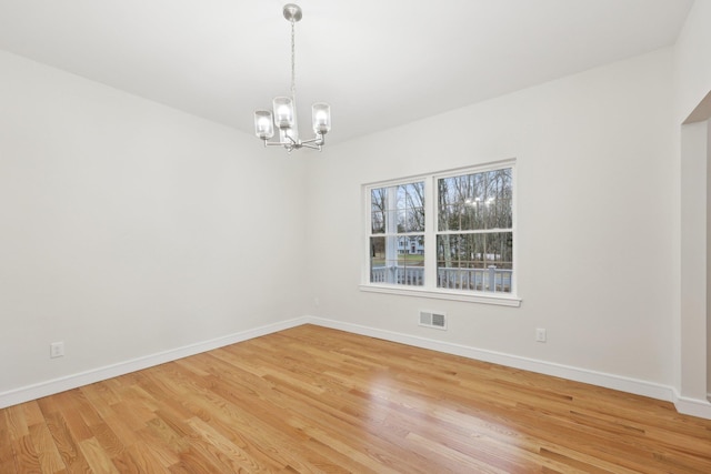 spare room featuring light wood finished floors, an inviting chandelier, visible vents, and baseboards