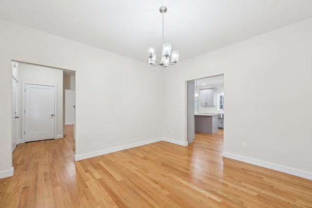 unfurnished room with light wood finished floors, a notable chandelier, and baseboards