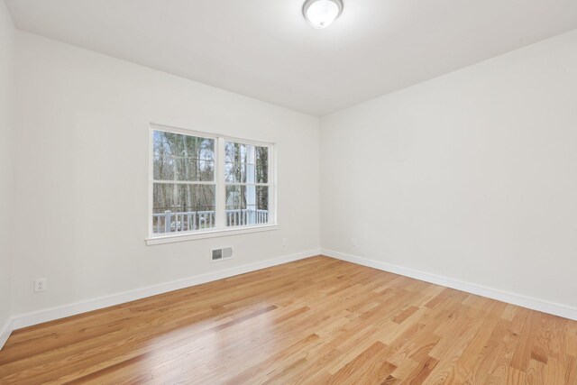 empty room with visible vents, light wood finished floors, and baseboards