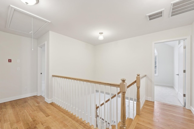 hallway with an upstairs landing, attic access, visible vents, and wood finished floors