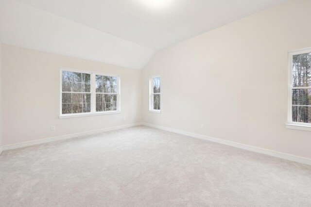 spare room with baseboards, lofted ceiling, and light colored carpet