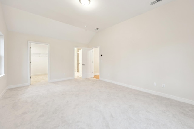 unfurnished bedroom with baseboards, vaulted ceiling, light colored carpet, and a spacious closet