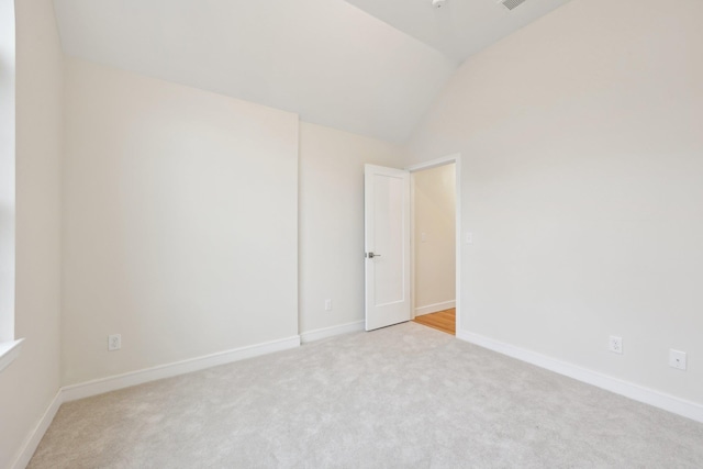 spare room featuring baseboards, light carpet, and vaulted ceiling
