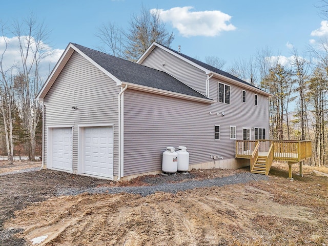 view of side of home featuring driveway, a deck, a shingled roof, and a garage