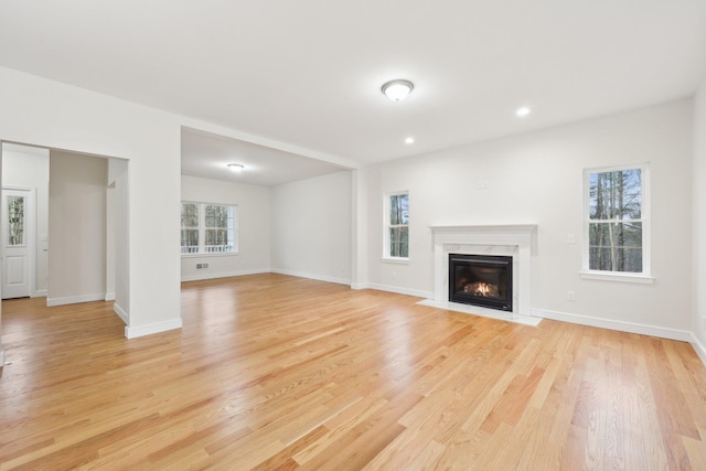 unfurnished living room with a high end fireplace, light wood-type flooring, and plenty of natural light