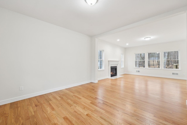 unfurnished living room with baseboards, visible vents, light wood-style floors, and a fireplace with flush hearth