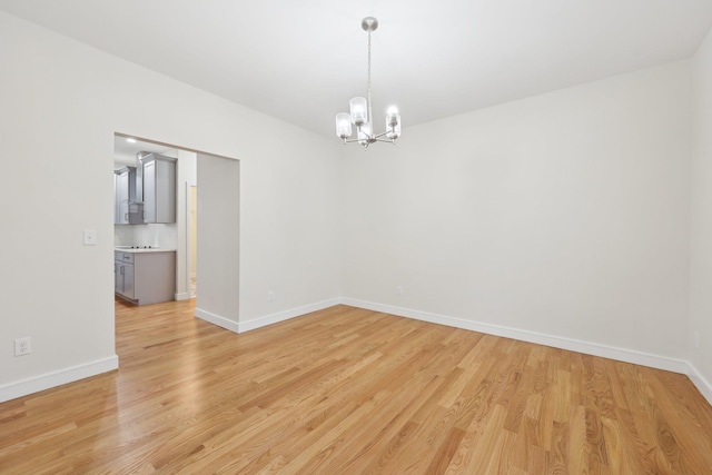 spare room featuring a chandelier, baseboards, and light wood finished floors