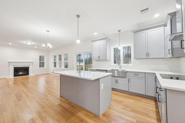 kitchen featuring wall chimney range hood, a sink, visible vents, gray cabinetry, and black electric cooktop