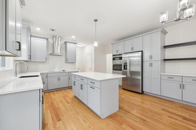 kitchen with a sink, appliances with stainless steel finishes, a center island, light wood finished floors, and wall chimney exhaust hood