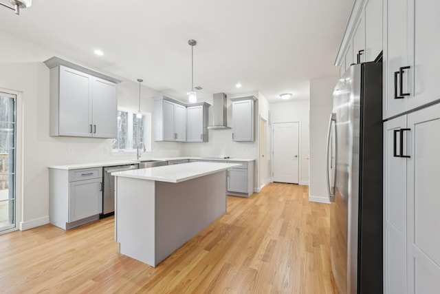 kitchen with a sink, stainless steel appliances, light wood-style floors, gray cabinets, and wall chimney exhaust hood
