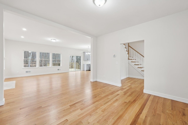 unfurnished living room featuring visible vents, stairway, light wood finished floors, and baseboards