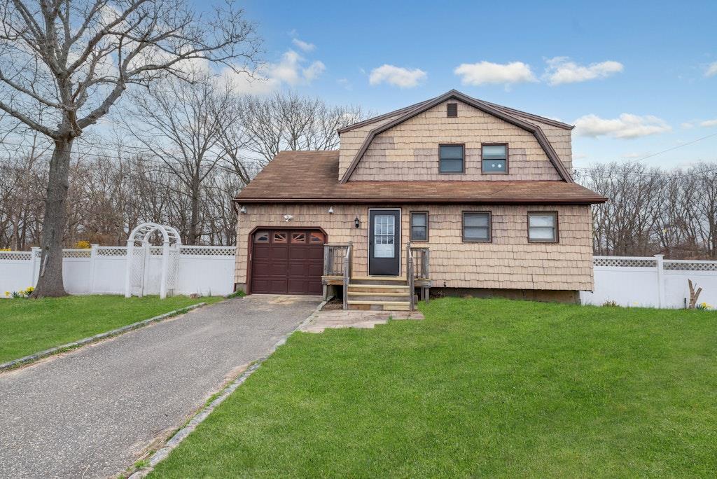 colonial inspired home featuring driveway, a front lawn, a garage, a gambrel roof, and fence