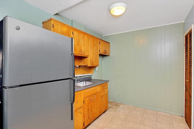 kitchen featuring freestanding refrigerator, light tile patterned flooring, dark countertops, brown cabinets, and a sink