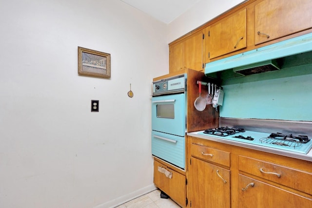 kitchen with oven, light countertops, under cabinet range hood, a warming drawer, and white gas stovetop